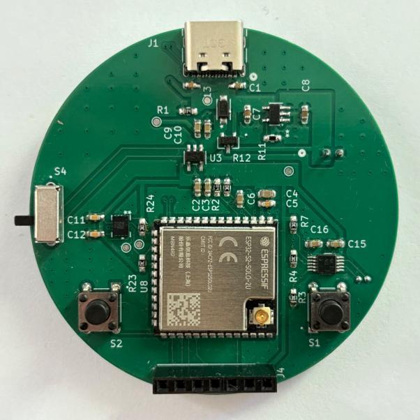 Photograph of the bare assembled PCB, a green round board with the ESP32-S2 module, USB-C connector, crystal, and buttons populated.